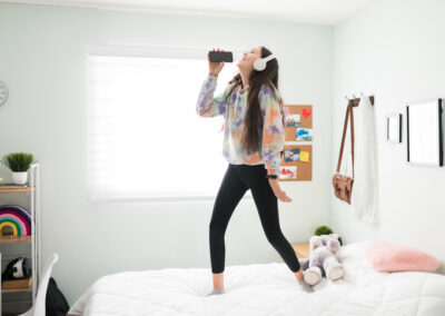 teen girl standing on her bedding australia bed playing karaoke with a phone and headphones